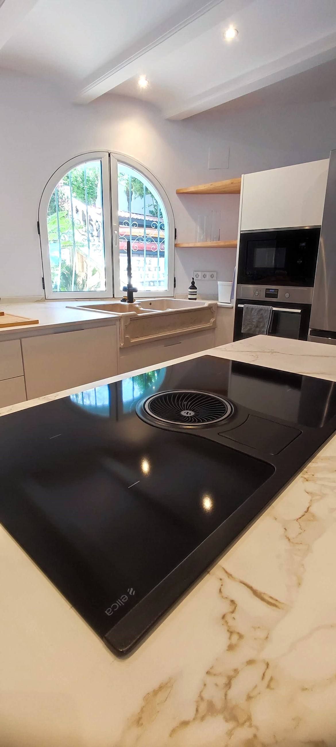 Placa de inducción con extracción integrada junto a fregadero de piedra en cocina a medida