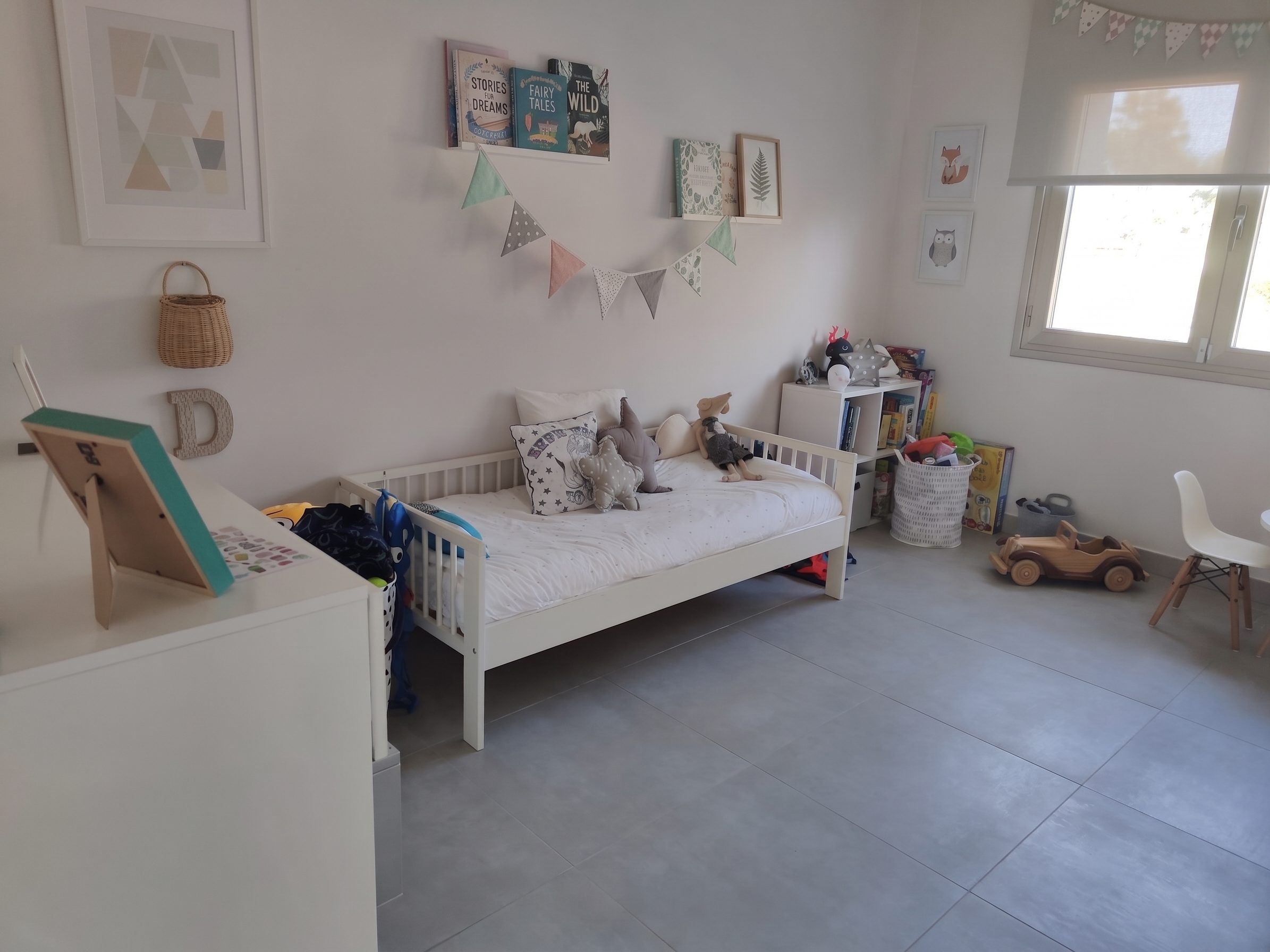 Habitación infantil con cama de barrotes, cómoda y juguetes por el suelo
