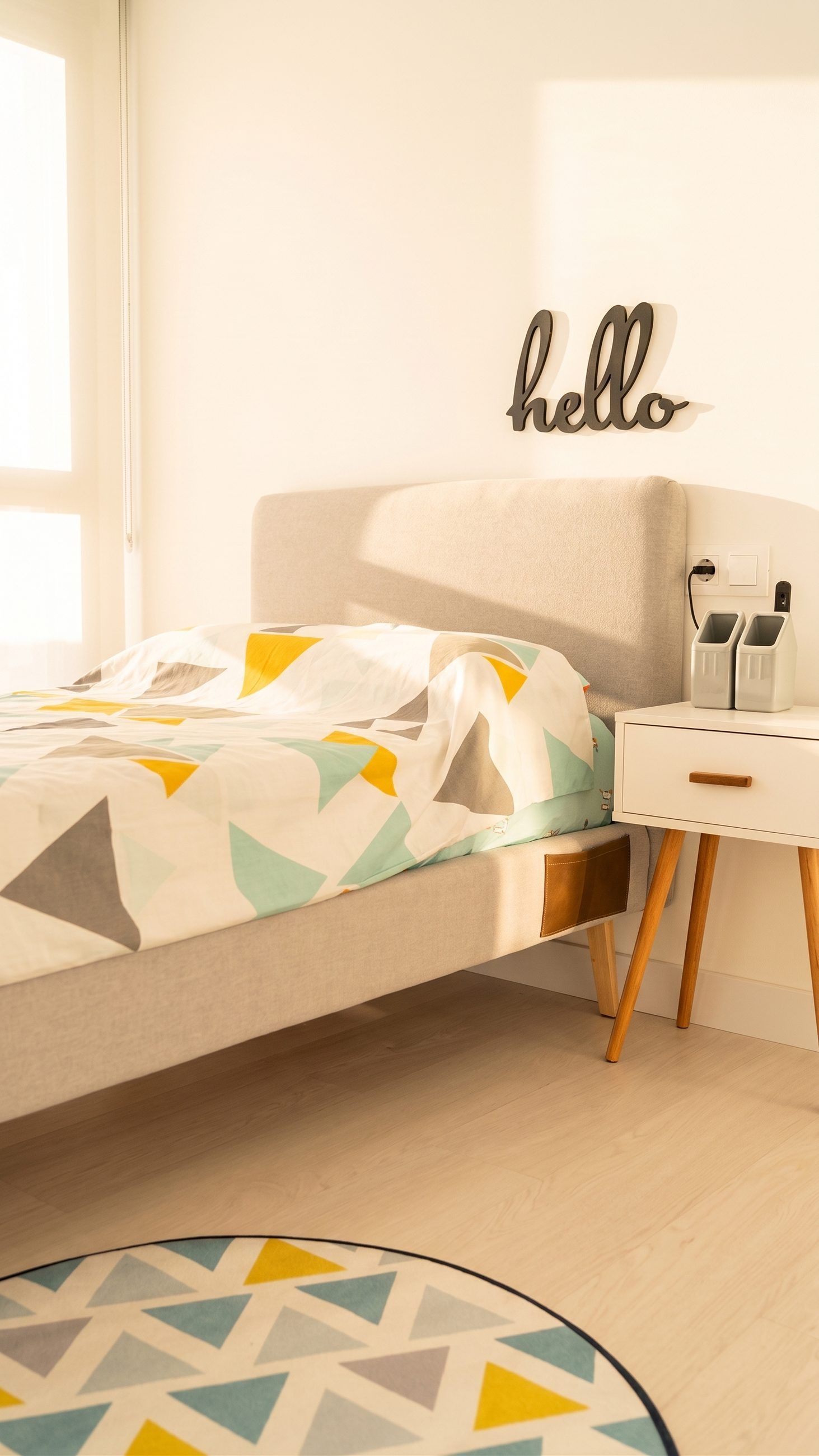 Cama tapizada con mesilla de patas de madera y luz natural en un dormitorio juvenil